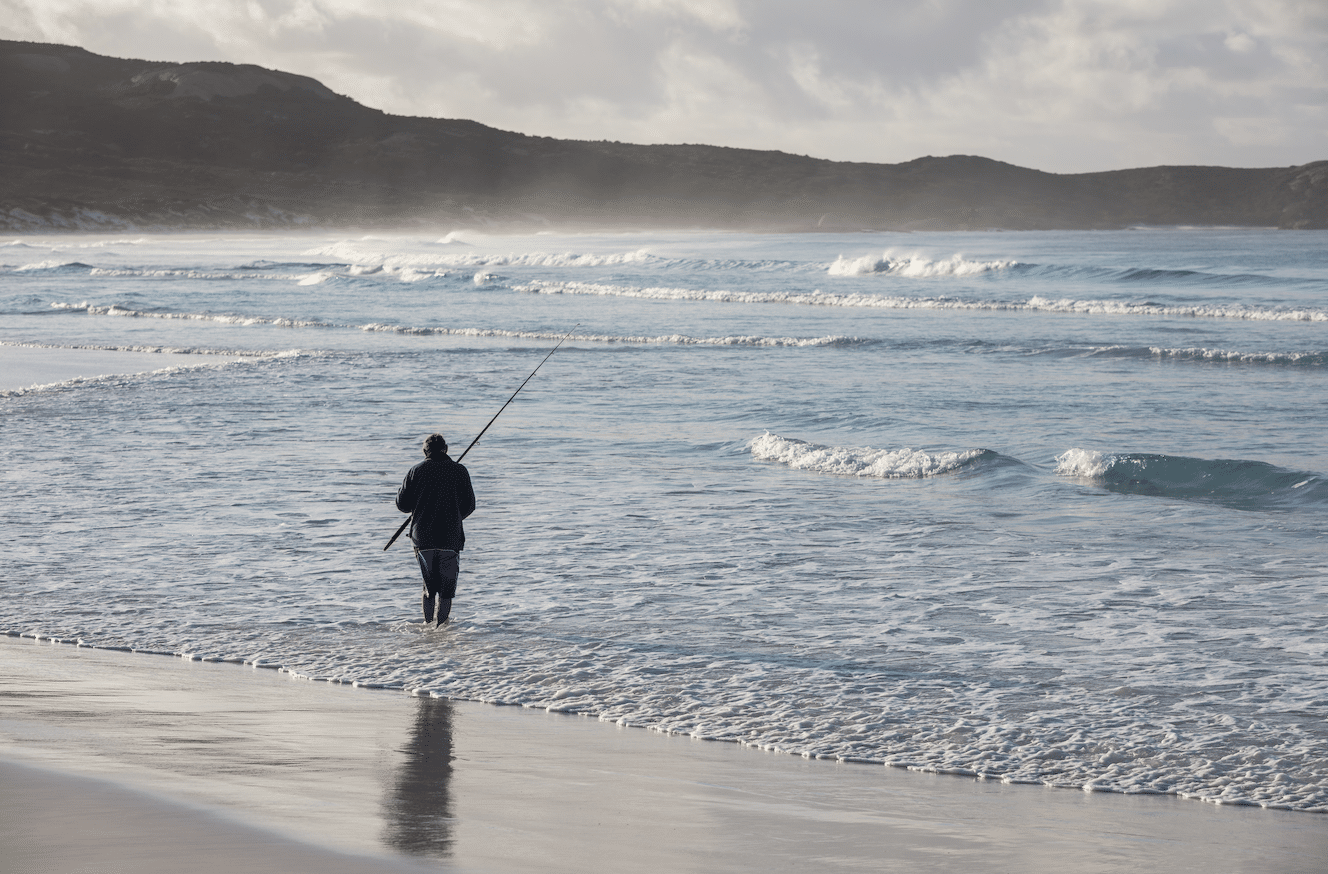 A fisherman in the water with a surf rod on a West Australian beach.